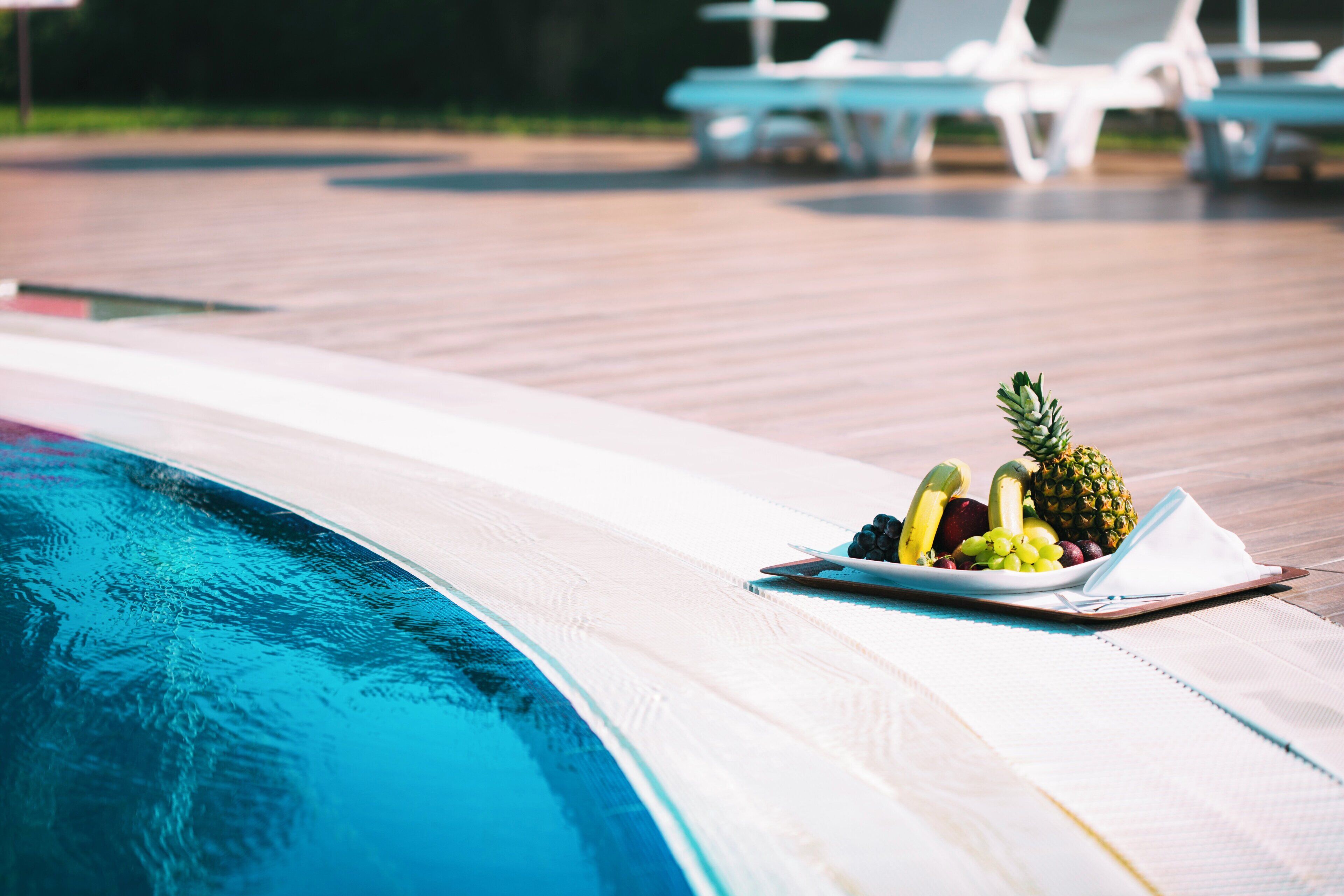 Zona junto a la piscina con una bandeja de frutas y sillones reclinables.