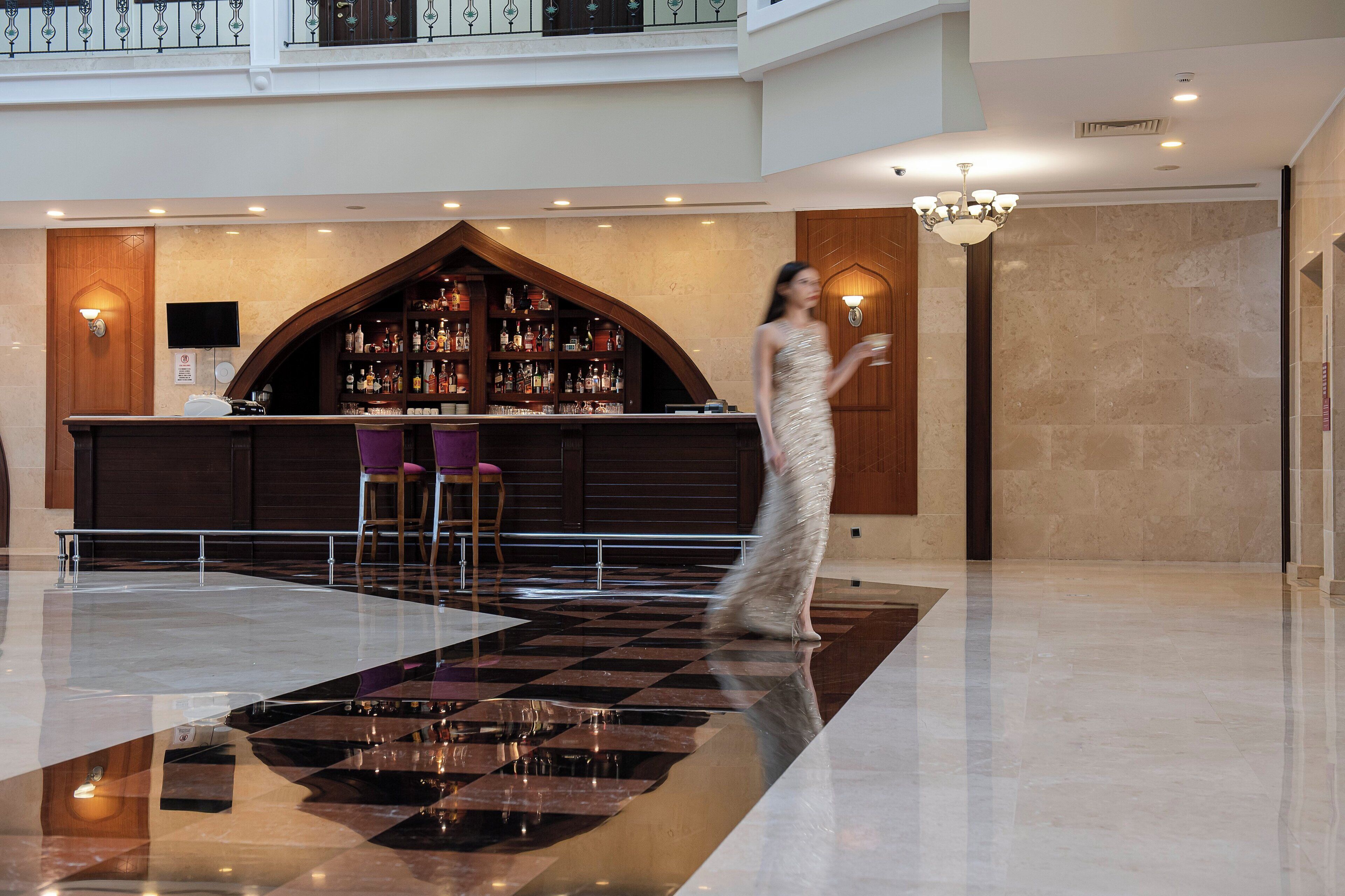 Un hall con piso a cuadros, una zona de bar con arco de madera y un candelabro.