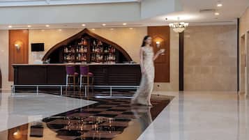 Un hall con piso a cuadros, una zona de bar con arco de madera y un candelabro.