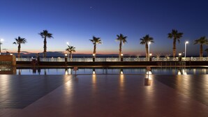 Un espace piscine éclairé la nuit, agrémenté de palmiers et de lampadaires.