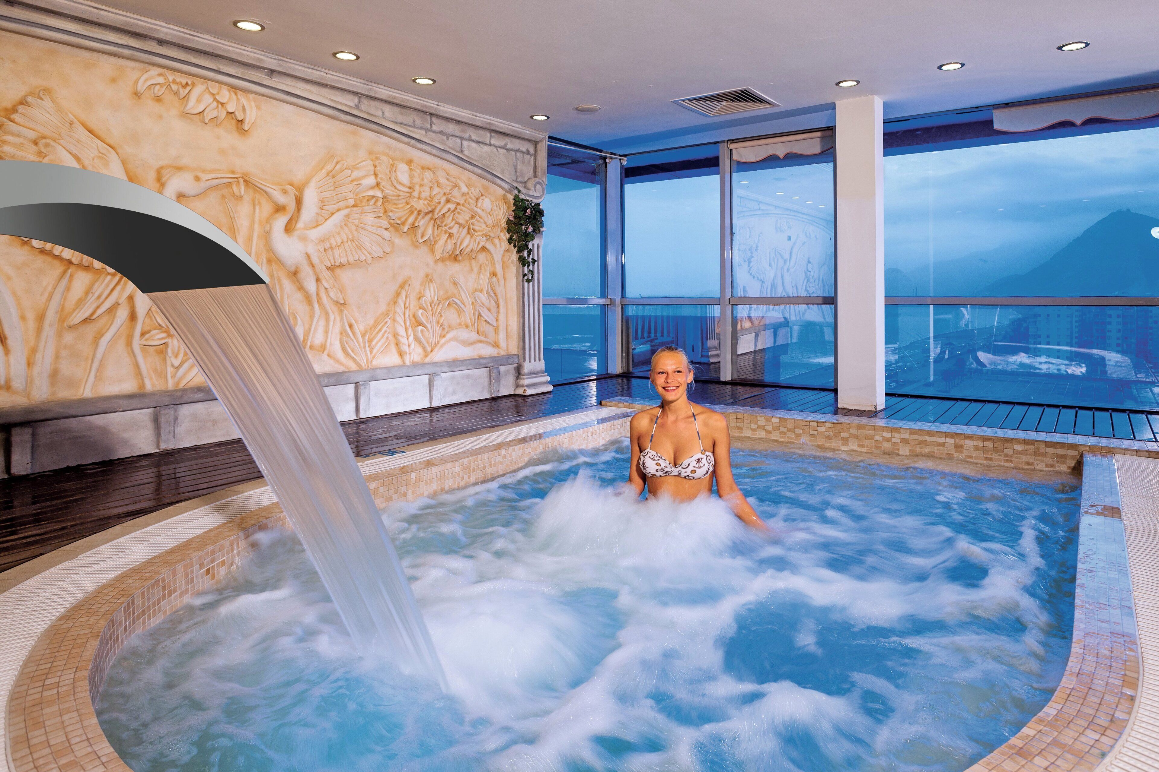 Eine Person in einer Hot-Tub mit Wasserfall, umgeben von einem großen Fenster mit Blick auf einen Berg.
