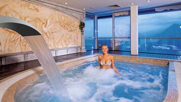 Eine Person in einer Hot-Tub mit Wasserfall, umgeben von einem großen Fenster mit Blick auf einen Berg.