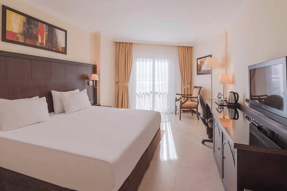 Habitación de hotel con una cama grande, un escritorio con televisión, una silla y una ventana con cortinas.