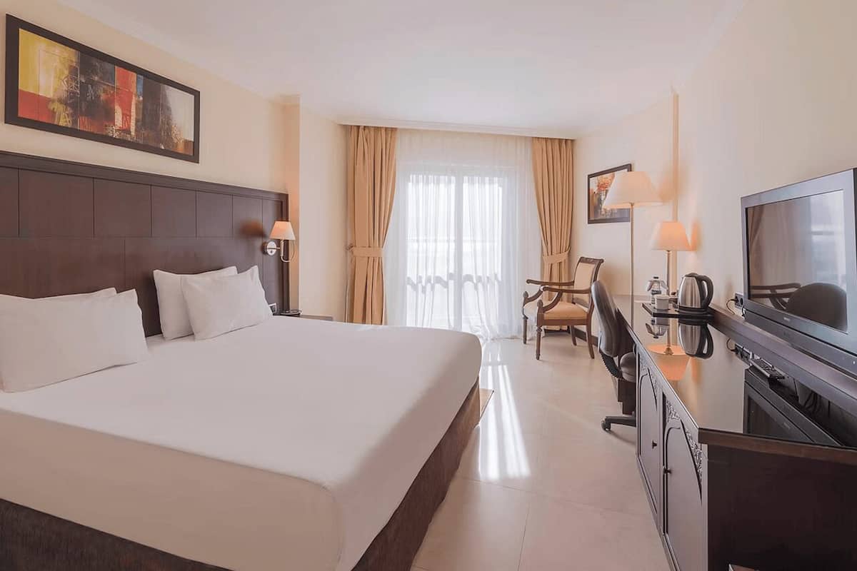 A hotel room with a large bed, a desk with a TV, a chair, and a window with curtains.
