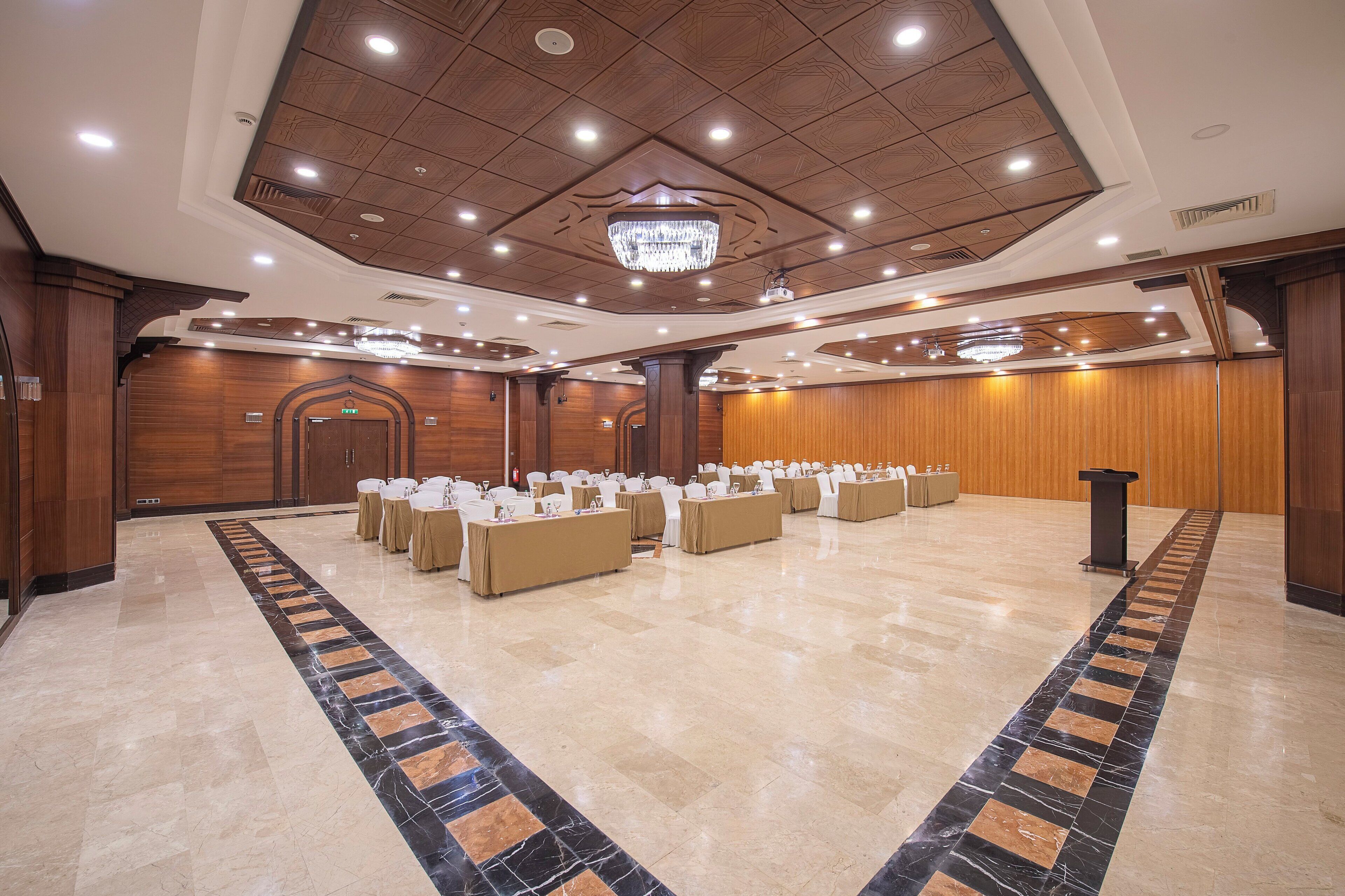Een ruime balzaal met een lange tafel gedekt voor evenementen, een kroonluchter en houten lambrisering.