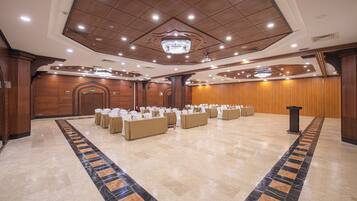 A spacious banquet hall with a long table set for events, a chandelier, and wooden paneling.