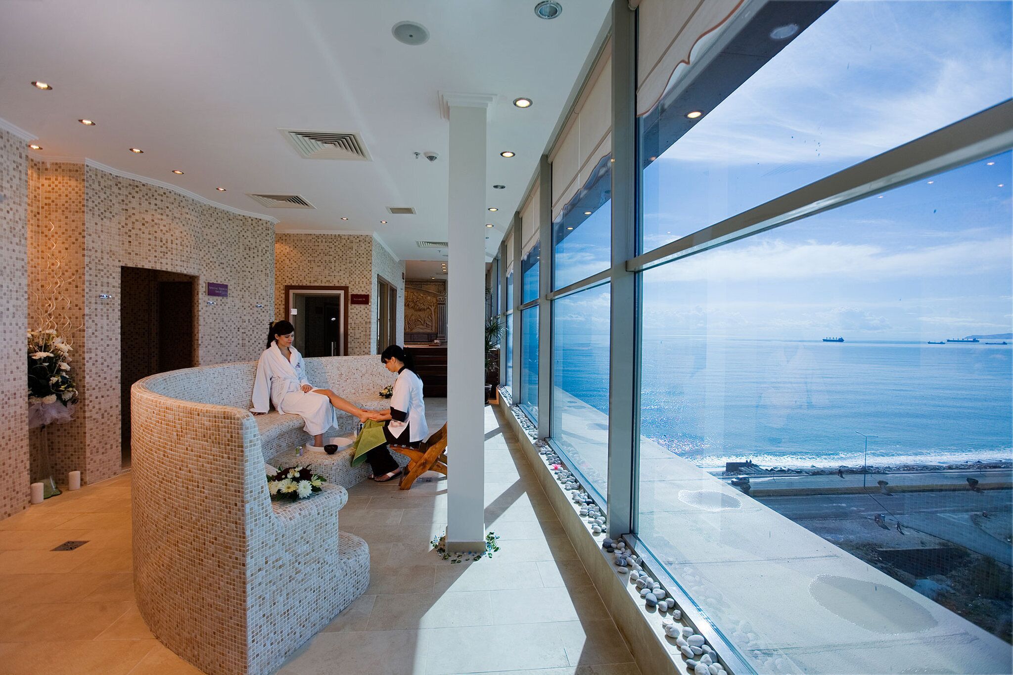 A reception area with a curved seating arrangement, large windows offering a view of the sea, and a tiled floor.