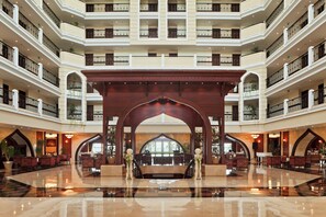 Un vestíbulo de hotel de varios niveles con un espacio central abierto, varios balcones y una imponente arcada de madera.