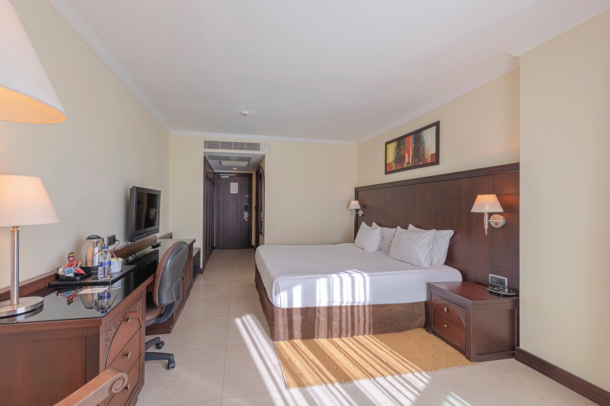 A hotel room with a bed, desk, TV, and lamps.