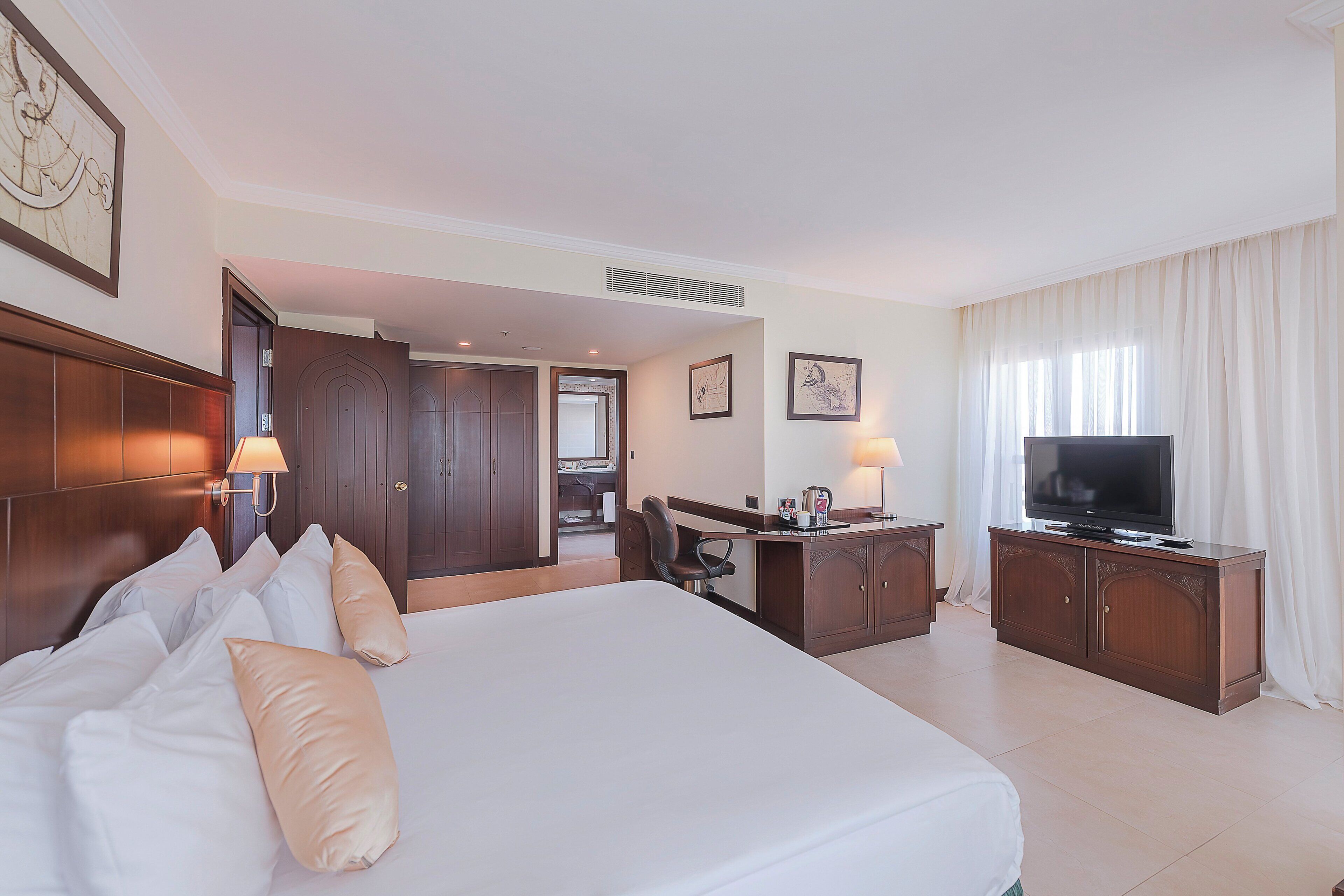 Habitación de hotel con una cama grande, un escritorio, televisión y baño visible a través de una puerta abierta.