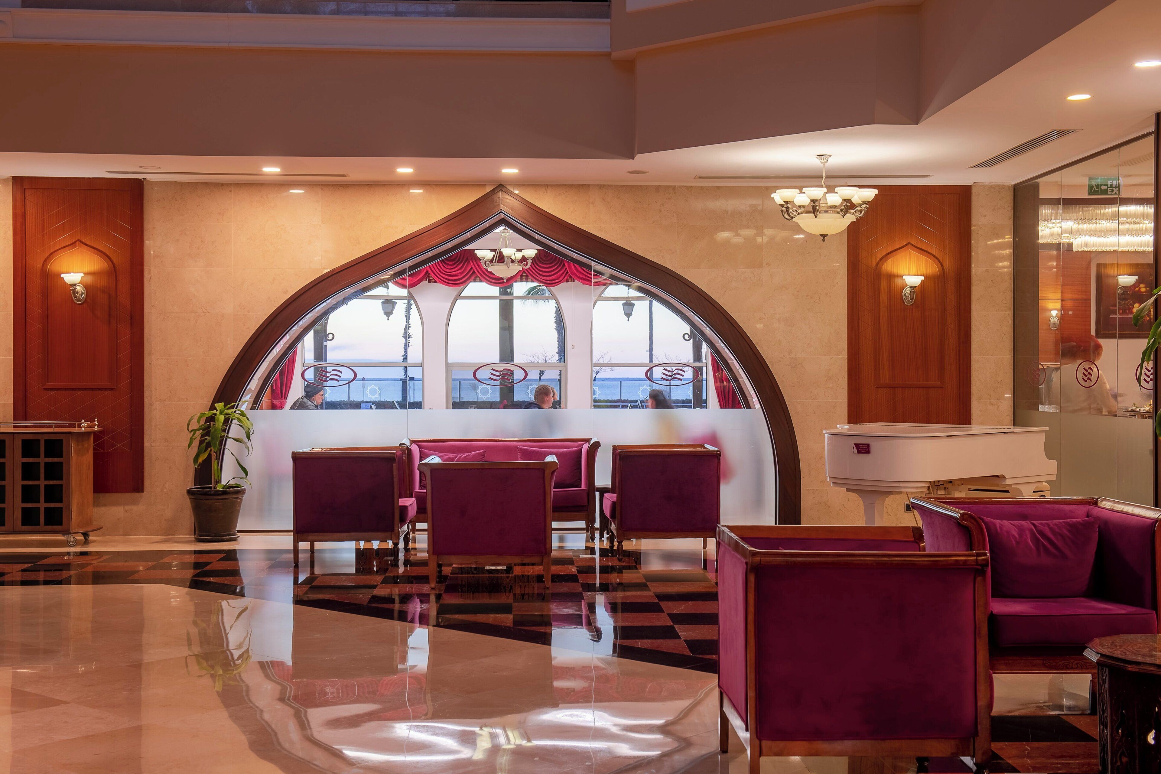 A lobby with a checkered floor, purple seating, a reception desk, and a large arched window with a view.
