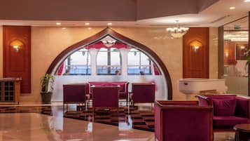 A lobby with a checkered floor, purple seating, a reception desk, and a large arched window with a view.