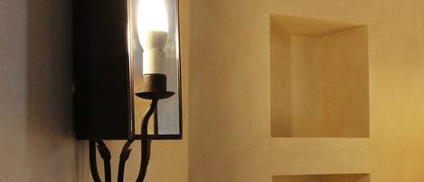 A wall-mounted light fixture with a candle-like bulb, three recessed shelves, and a dark-colored panel.