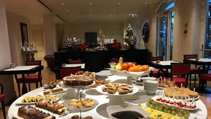 En buffetbod med forskellige desserter og frugter, et juletræ og et klaver i baggrunden.