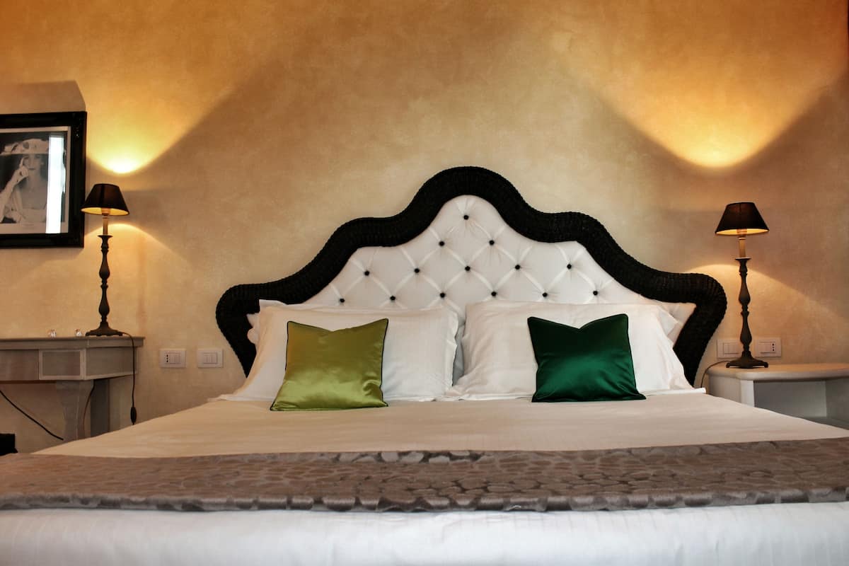 Una cama bien hecha con cabecera capitonada, dos lámparas de noche y un cuadro en la pared.