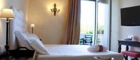 A hotel room with a bed, a desk, a chair, a lamp, a TV, and a window with curtains.