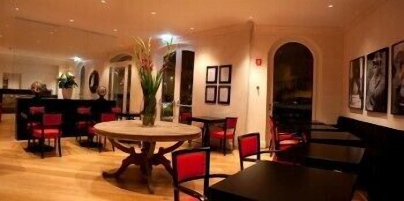 A dining area with round tables and red chairs, a central floral arrangement, and framed artwork on the walls.
