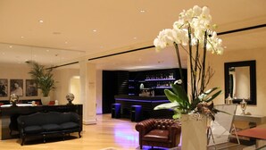 En moderne hotellobby med et barområde, en sort lædersofa, en brun læderlænestol og en stor hvid orchidé.