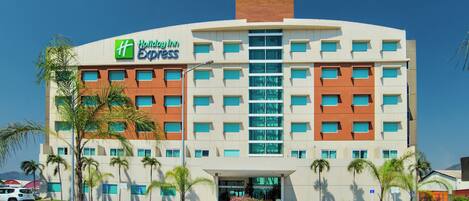 A Holiday Inn Express hotel with a modern design, featuring a central entrance, multiple floors, and a parking area with palm trees.