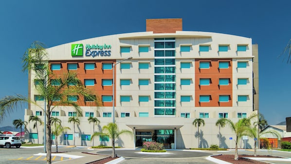 A Holiday Inn Express hotel with a modern design, featuring a central entrance, multiple floors, and a parking area with palm trees.
