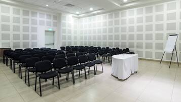 Una sala de conferencias con filas de sillas, una mesa blanca y una pantalla de proyecciones.