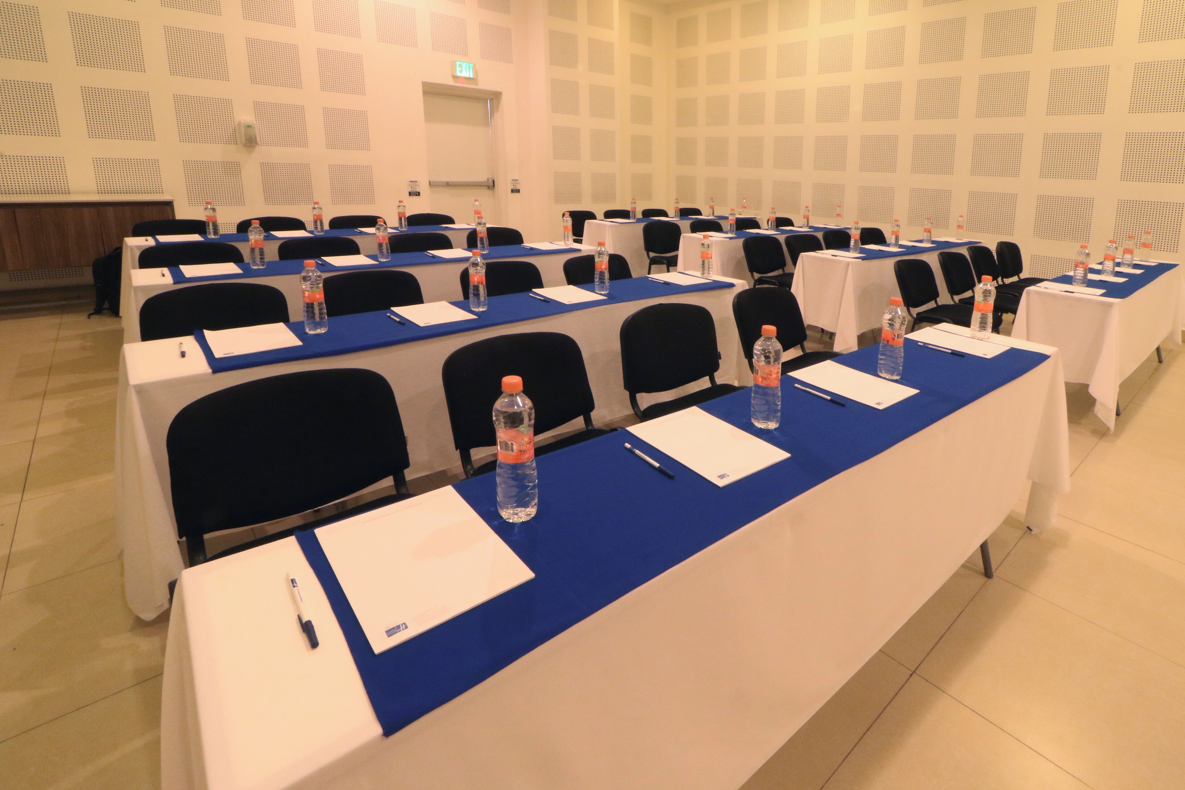 A conference room with multiple tables, each equipped with water bottles, notepads, and pens.