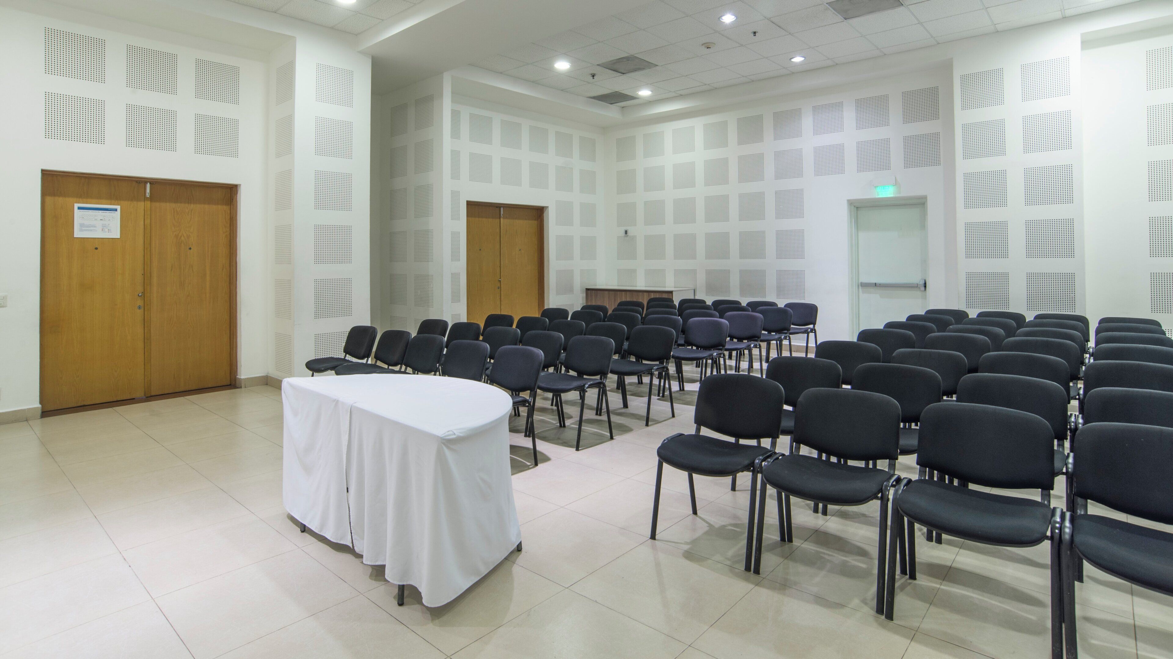 A conference room with rows of chairs, a white table, and soundproofing panels on the walls.