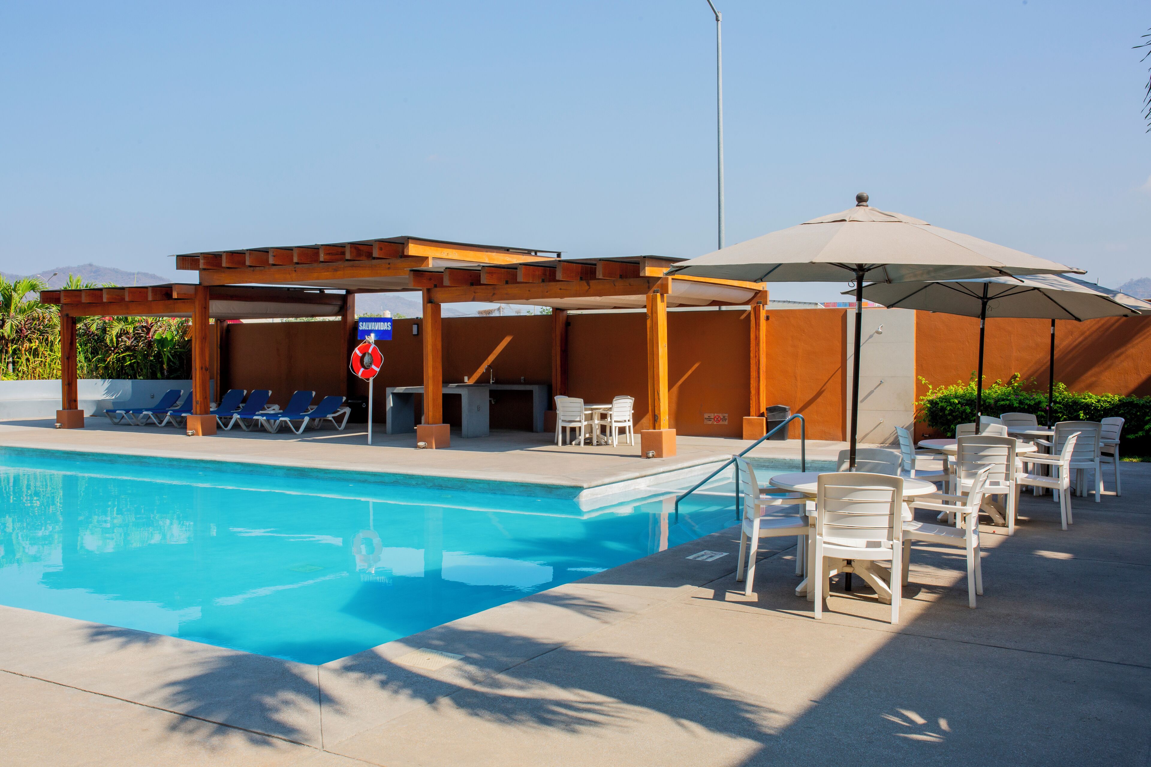 Ein Pool mit Liegestühlen, einer überdachten Sitzgruppe und einem Rettungsschwimmer-Schild.