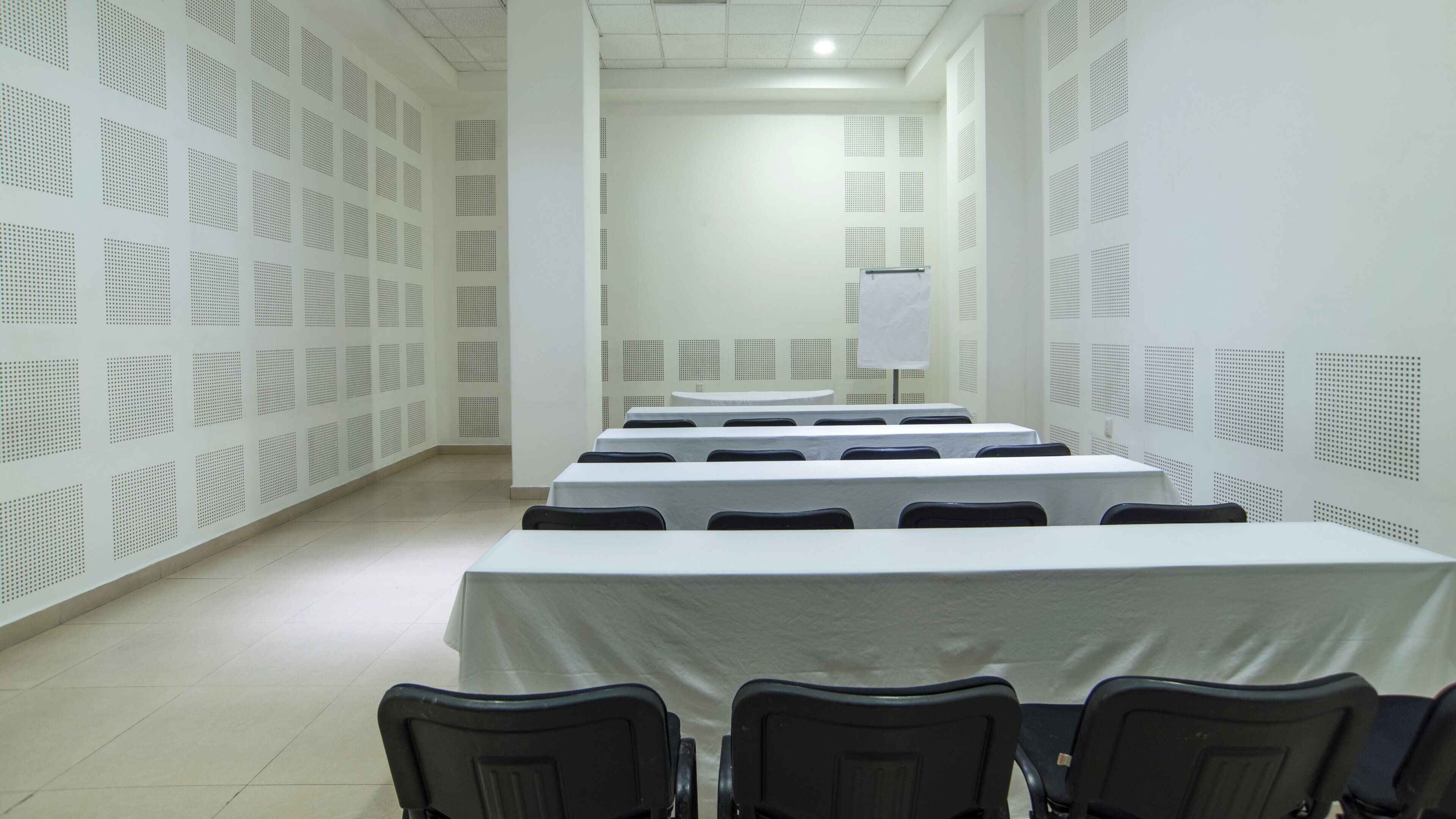 Ein Konferenzraum mit Tischen und Stühlen, weißen Wänden mit Akustikpaneelen und einer Whiteboard-Fläche.
