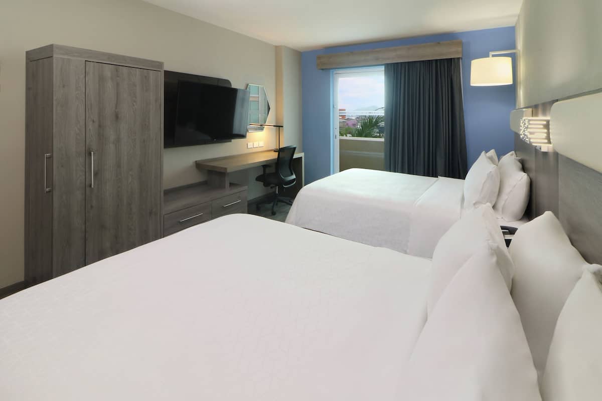 Habitación de hotel con dos camas, un escritorio, un televisor y una ventana con vistas.