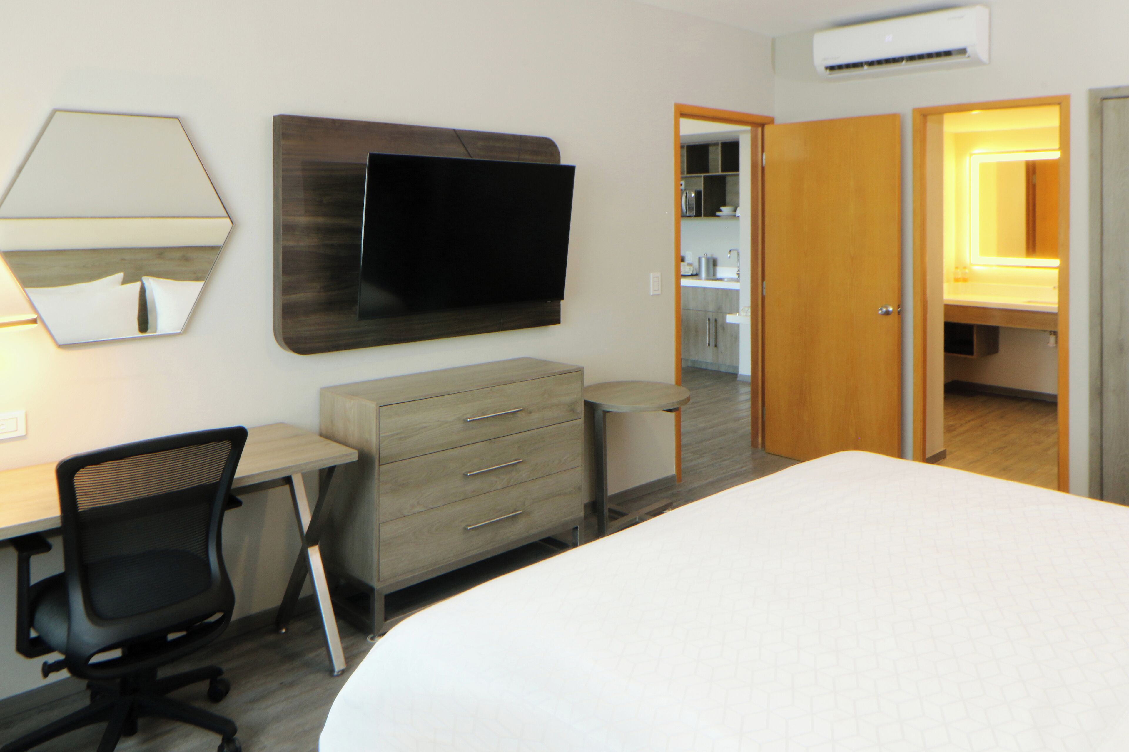 Habitación de hotel con cama, un escritorio con silla, televisor montado en la pared, espejo y armario.