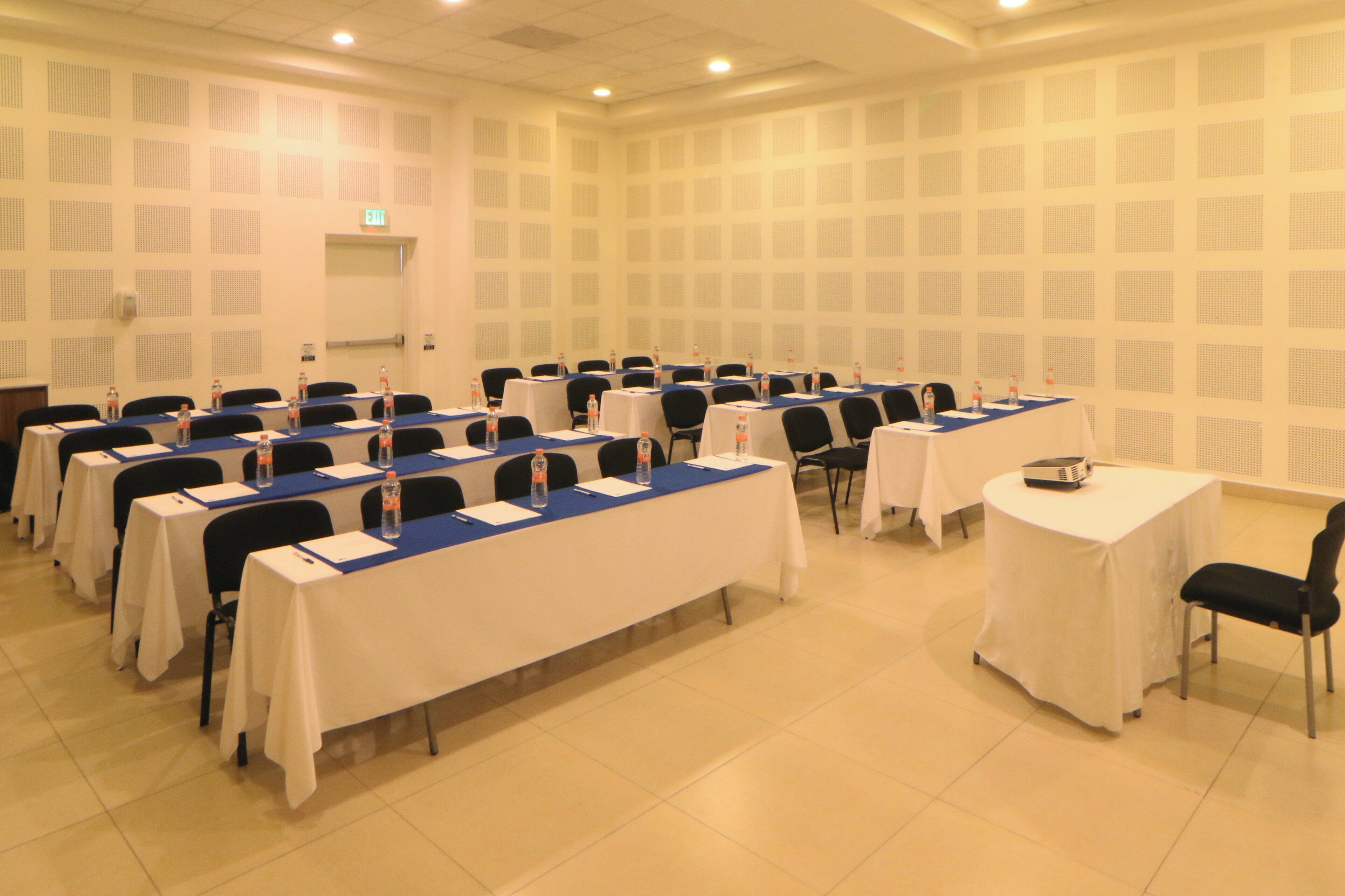 Un salón de conferencias con varias mesas y sillas, equipado con botellas de agua y tarjetas de identificación.