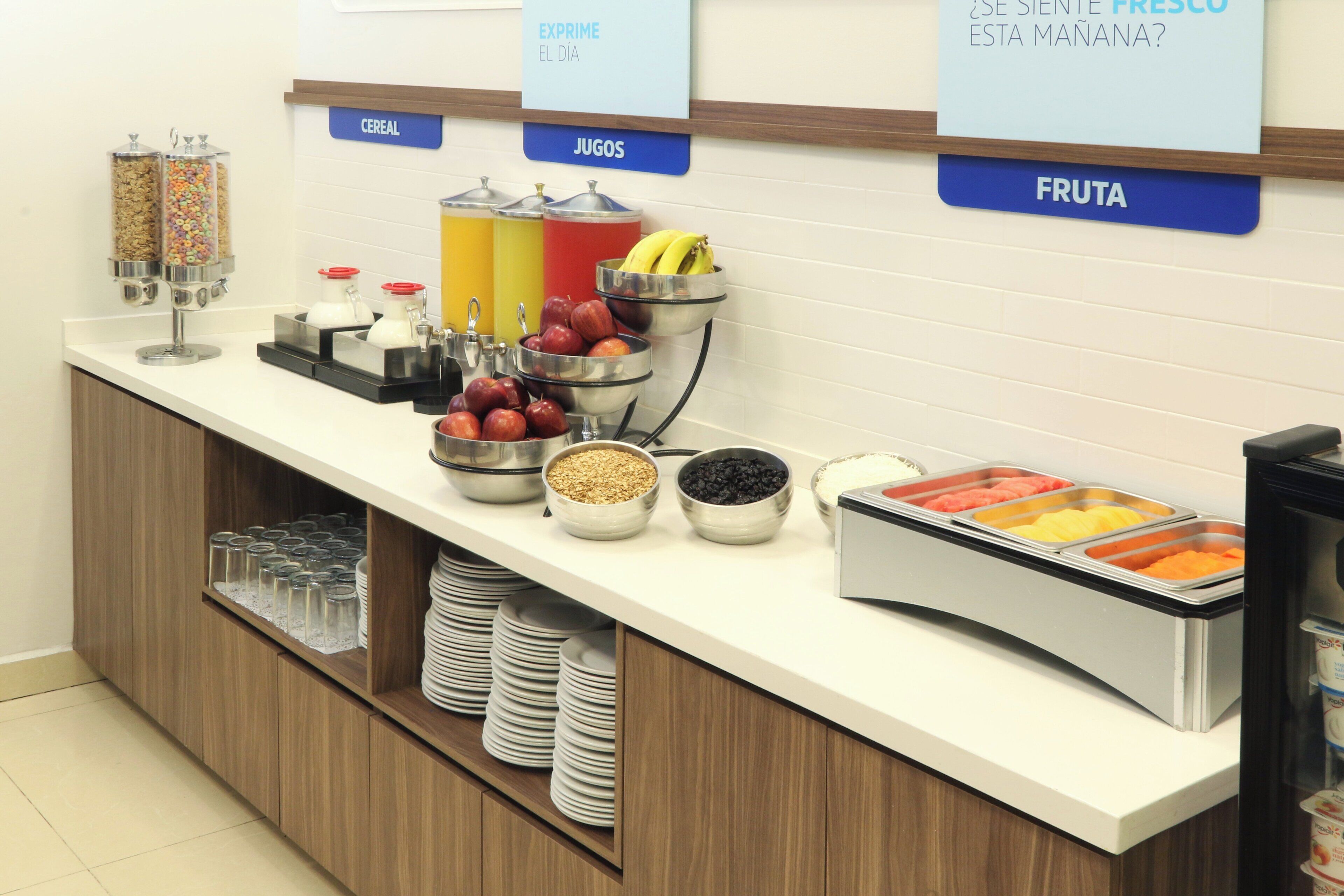 A breakfast buffet with labeled sections for cereal, juices, fruits, and yogurt.