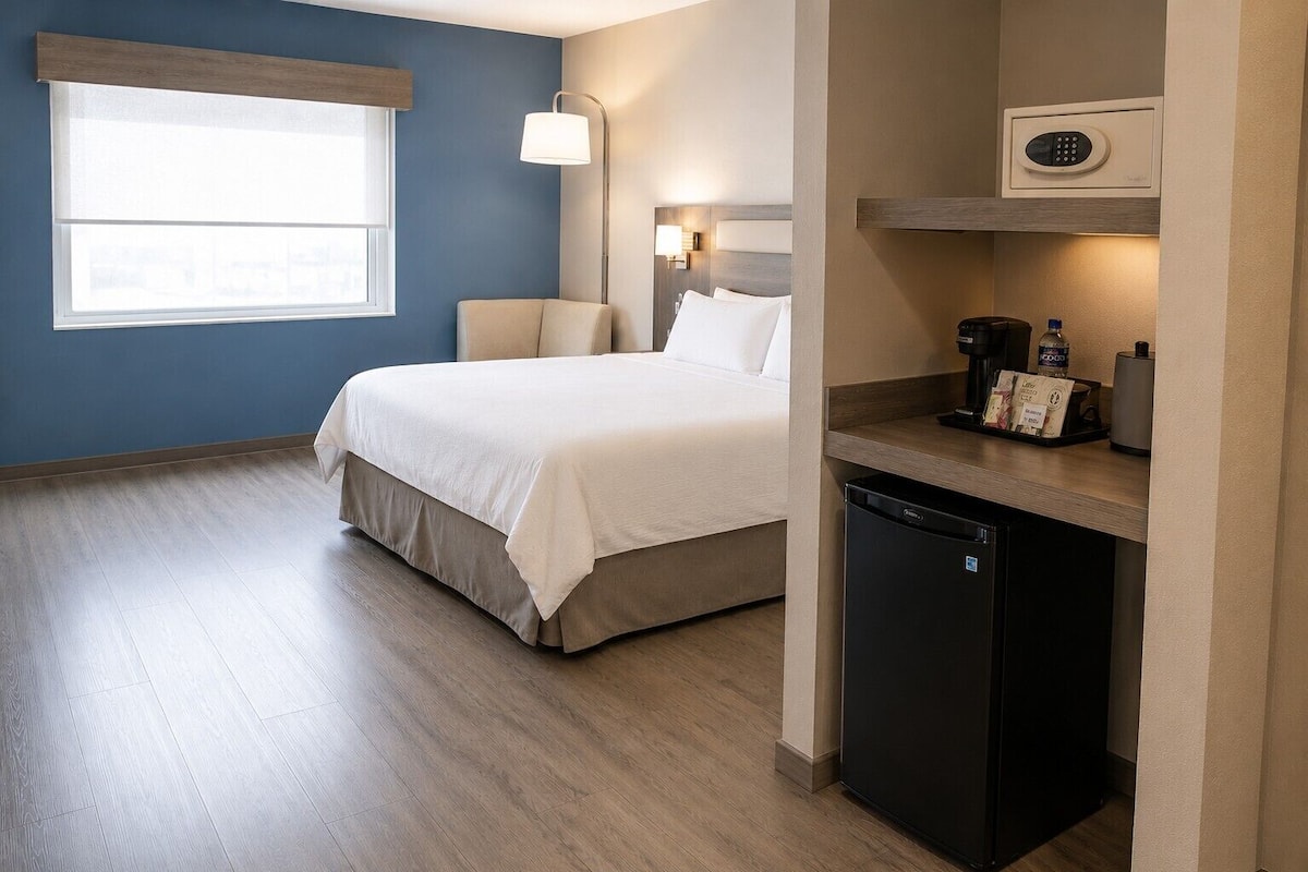 Habitación de hotel con cama, lámpara de noche, una pequeña cocina americana con cafetera y microondas.