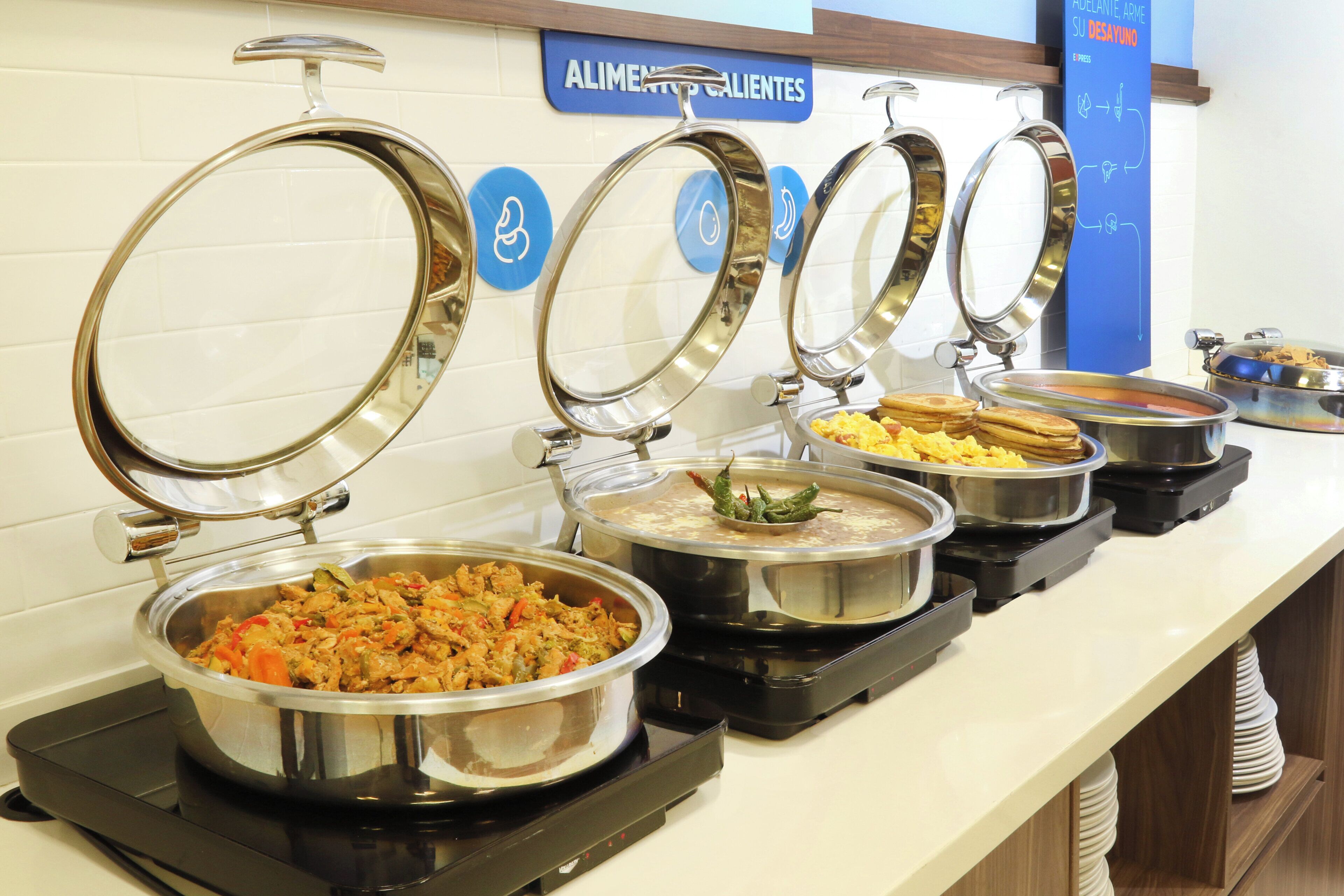 A buffet area with multiple food stations, each with a lid and labeled with a blue sign.