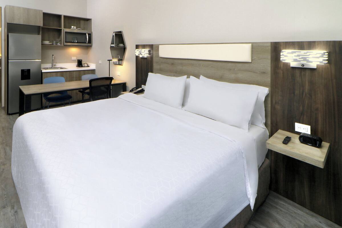 Habitación de hotel con una cama grande, un escritorio con silla, un microondas y un estante pequeño con un teléfono y un control remoto.