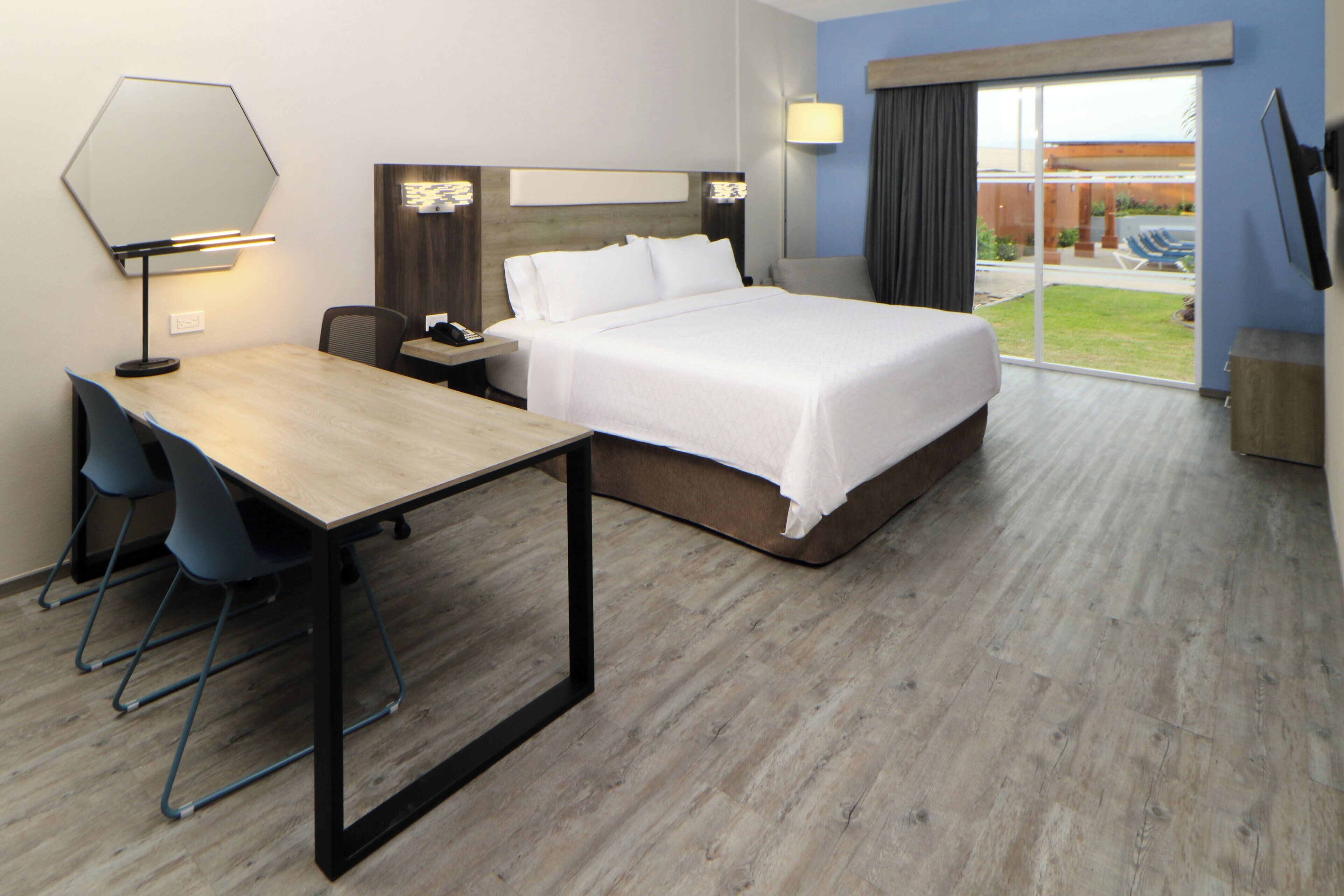 Une chambre d’hôtel équipée d’un lit, d’un bureau, de chaises, d’un miroir et offrant une vue sur l’extérieur.