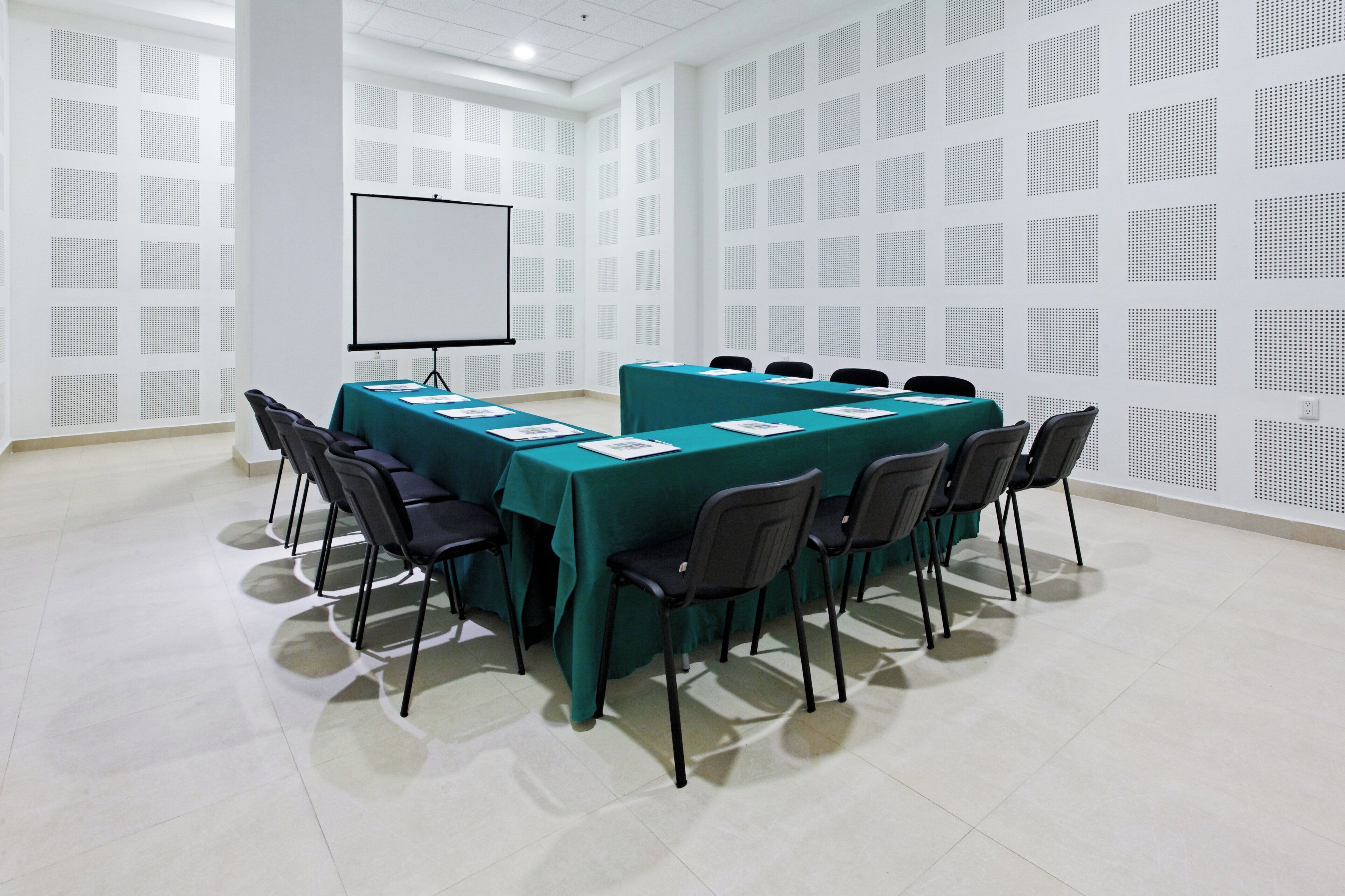 A conference room with a whiteboard, teal tablecloths, and black chairs.