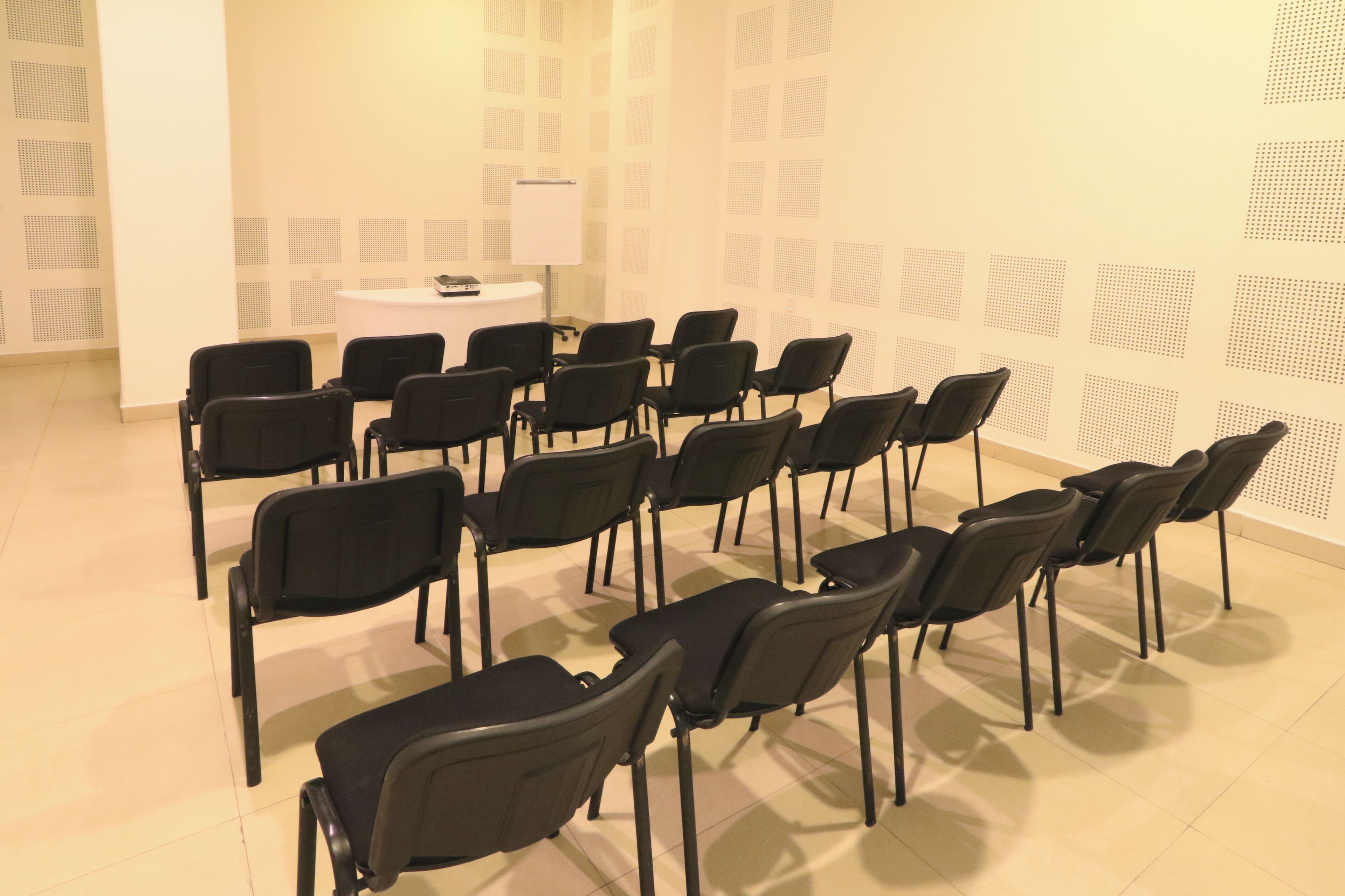 Ein Konferenzraum mit Reihen schwarzer Stühle, einer Tafel und einem kleinen Tisch mit einem Laptop.