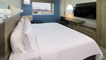 Quarto de hotel com uma cama grande, uma escrivaninha com televisão, uma cadeira e uma janela com vista para uma ponte.