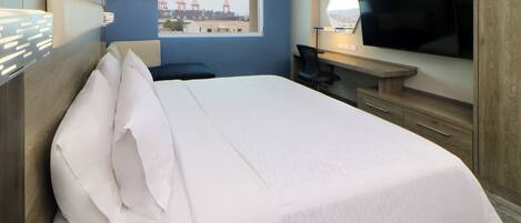 Habitación de hotel con una cama grande, un escritorio con televisor, una silla y una ventana con vistas a un puente.