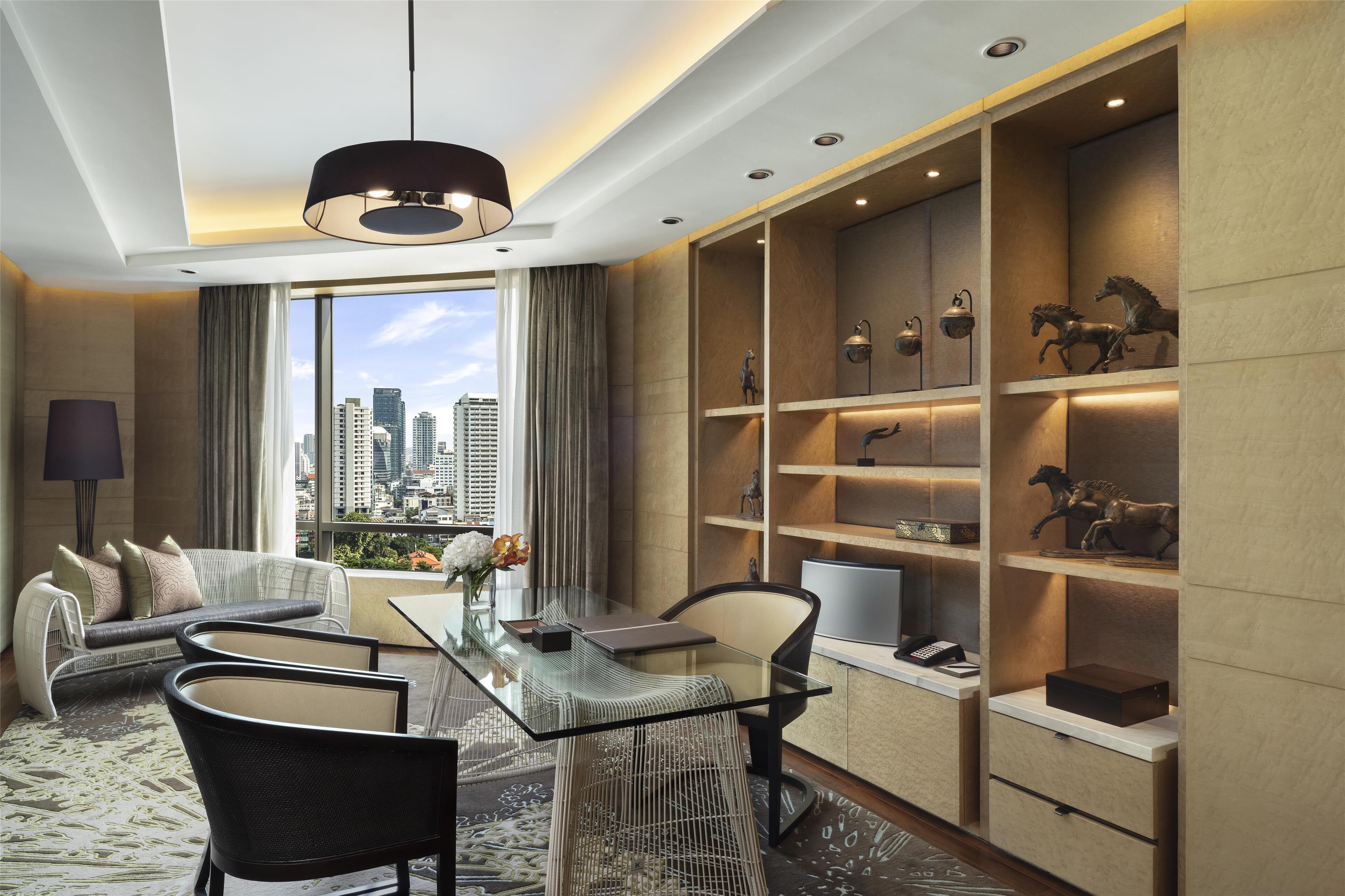 A modern hotel room with a glass dining table, comfortable seating, a city view, and decorative shelves.