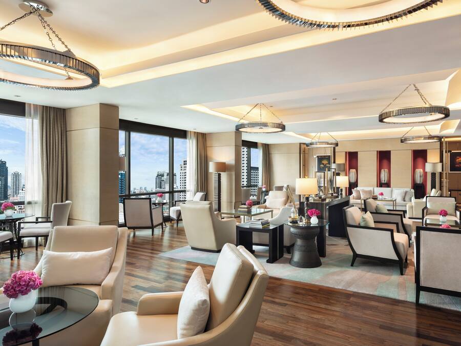 A spacious hotel lobby with multiple seating areas, large windows offering city views, and modern lighting fixtures.
