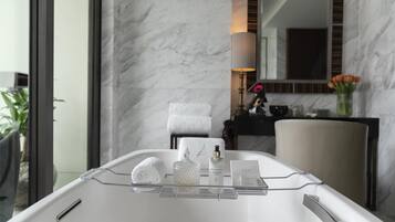A bathroom with a marble wall, a towel rack, a bottle of skincare product, and a tray with a towel and a glass container.