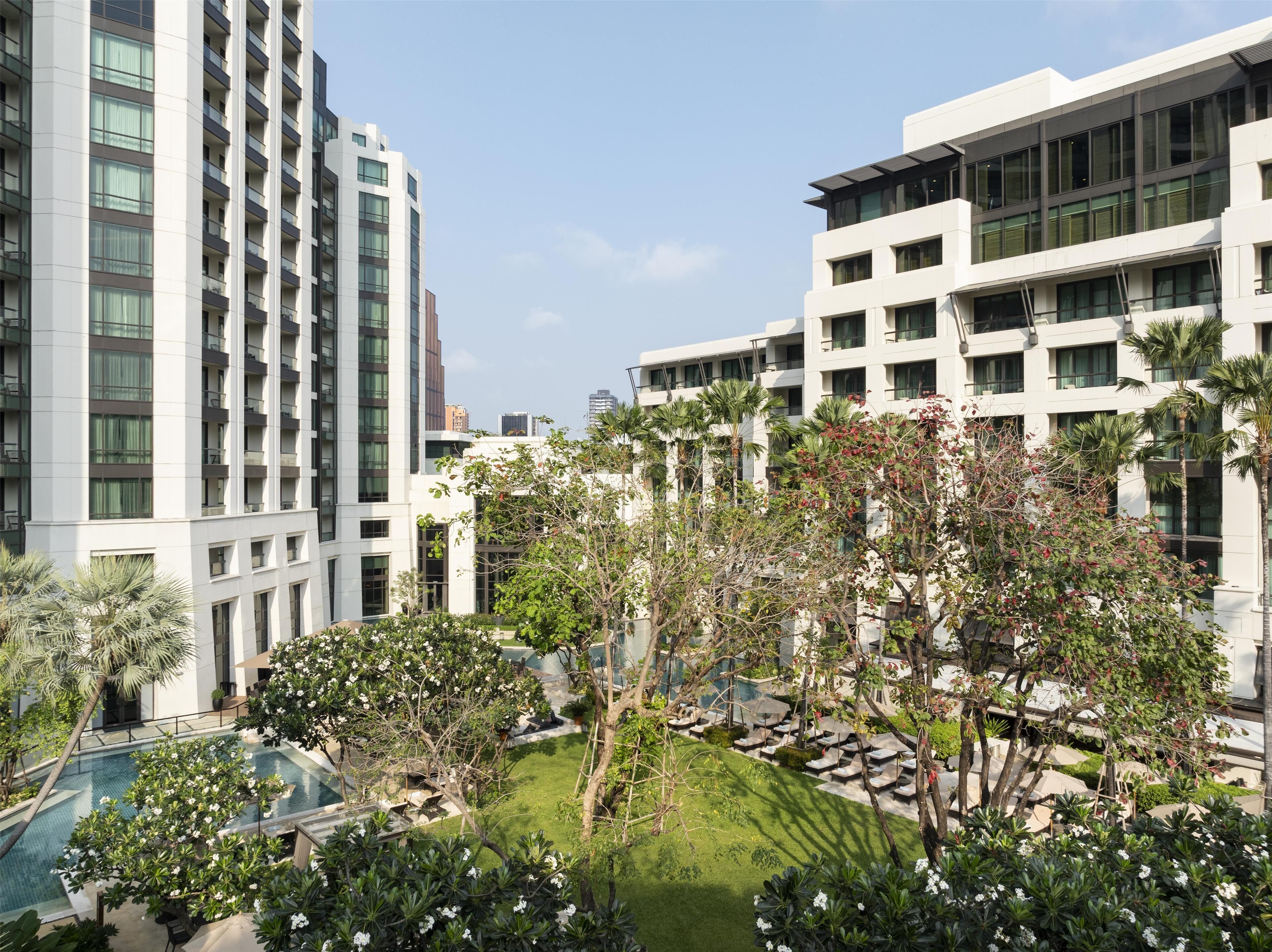 Un hotel moderno con varias plantas, una piscina en la azotea y jardines exuberantes.