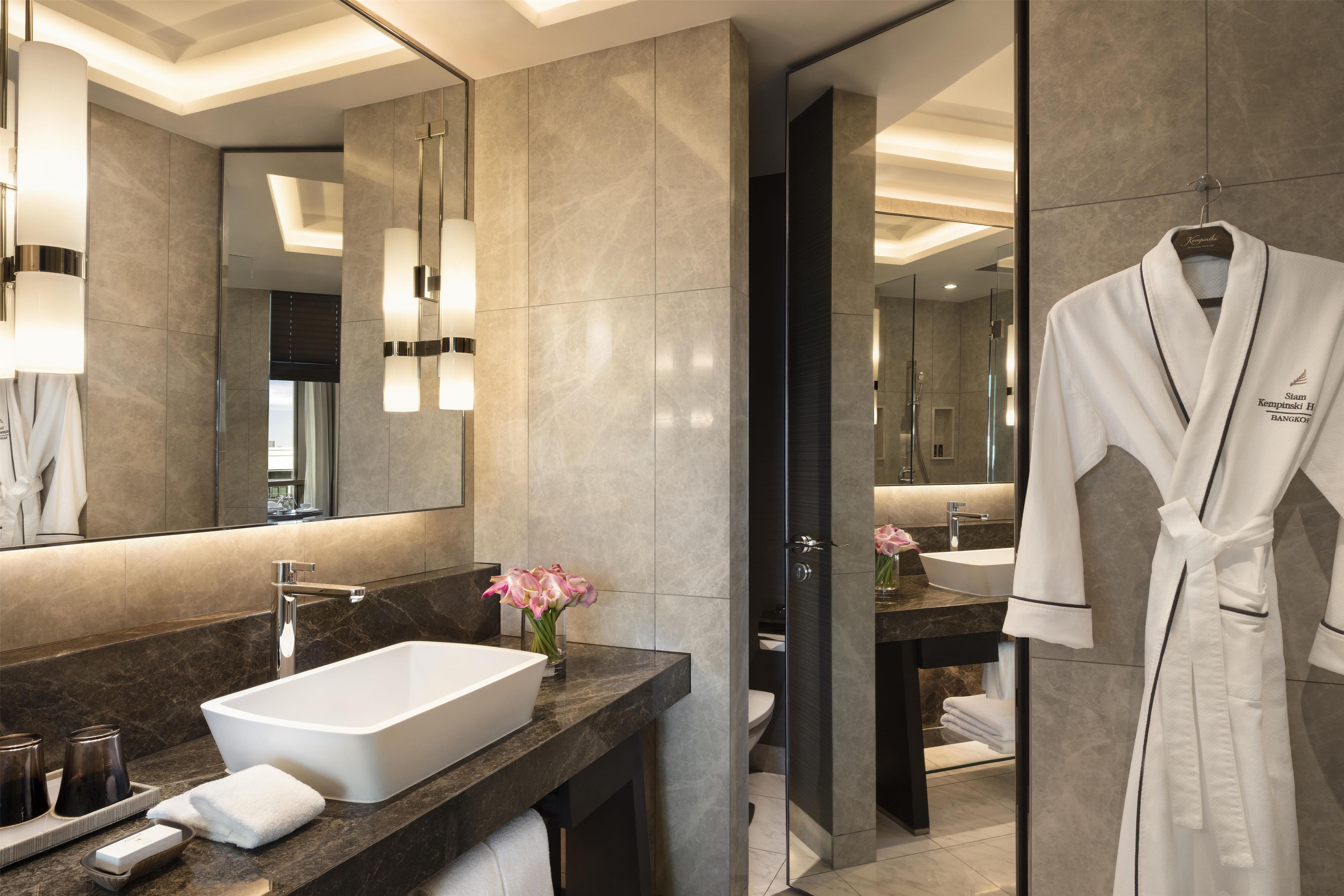 A modern bathroom with a large mirror, a white bathtub, a marble countertop, and a robe hanging on a rack.