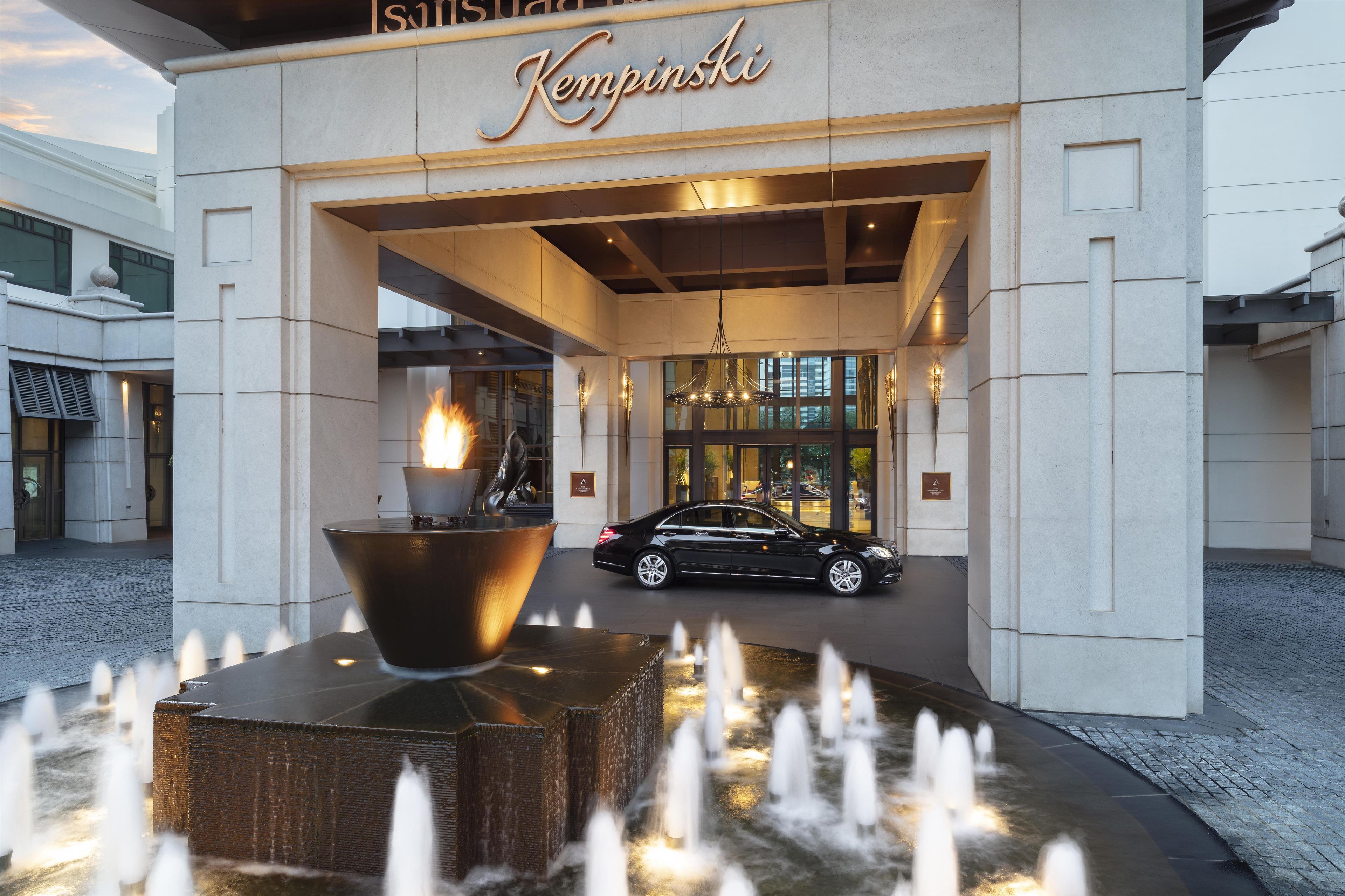 Entrada de un hotel con un letrero grande iluminado, un elemento decorativo de fuego y una fuente.