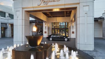 Entrada de un hotel con un letrero grande iluminado, un elemento decorativo de fuego y una fuente.