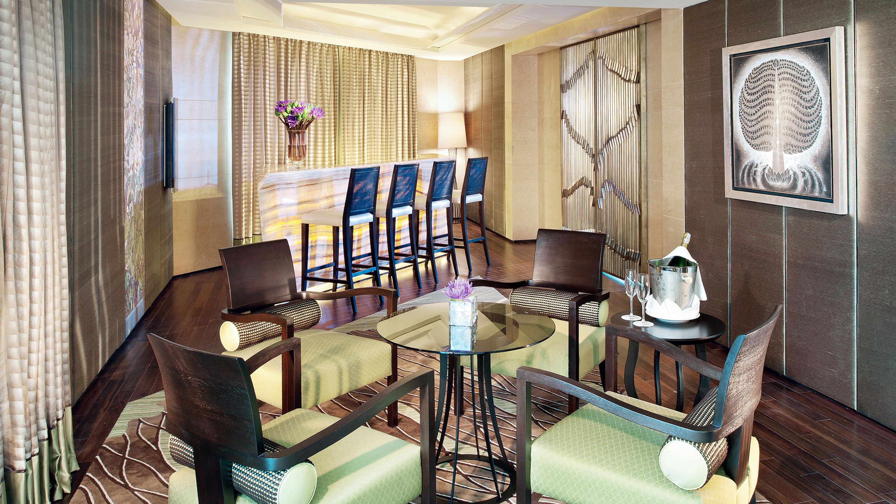 A hotel room with a dining area featuring a glass table, four chairs, and a decorative wall piece.