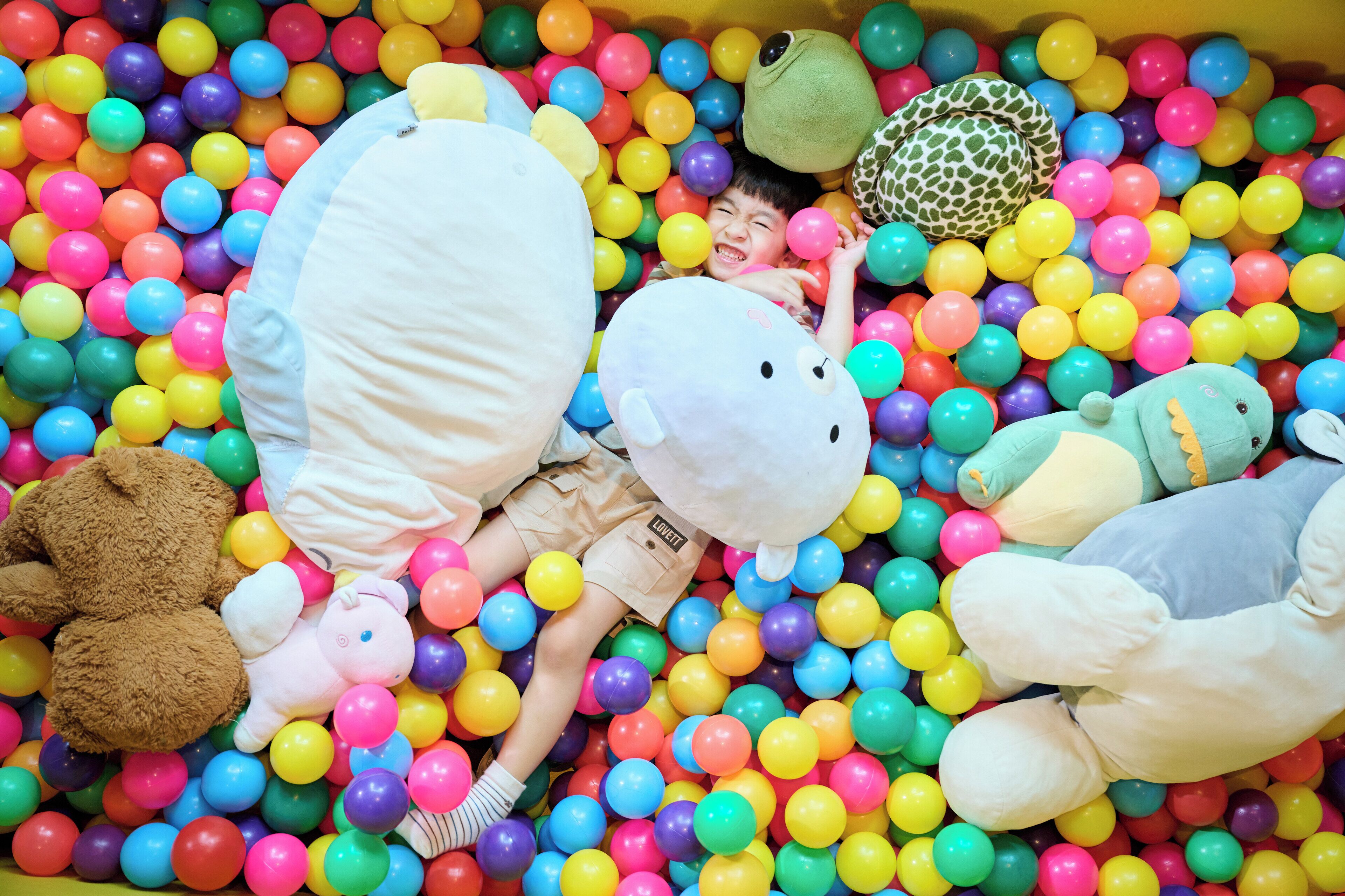 A child surrounded by colorful plastic balls and plush toys in a play area.